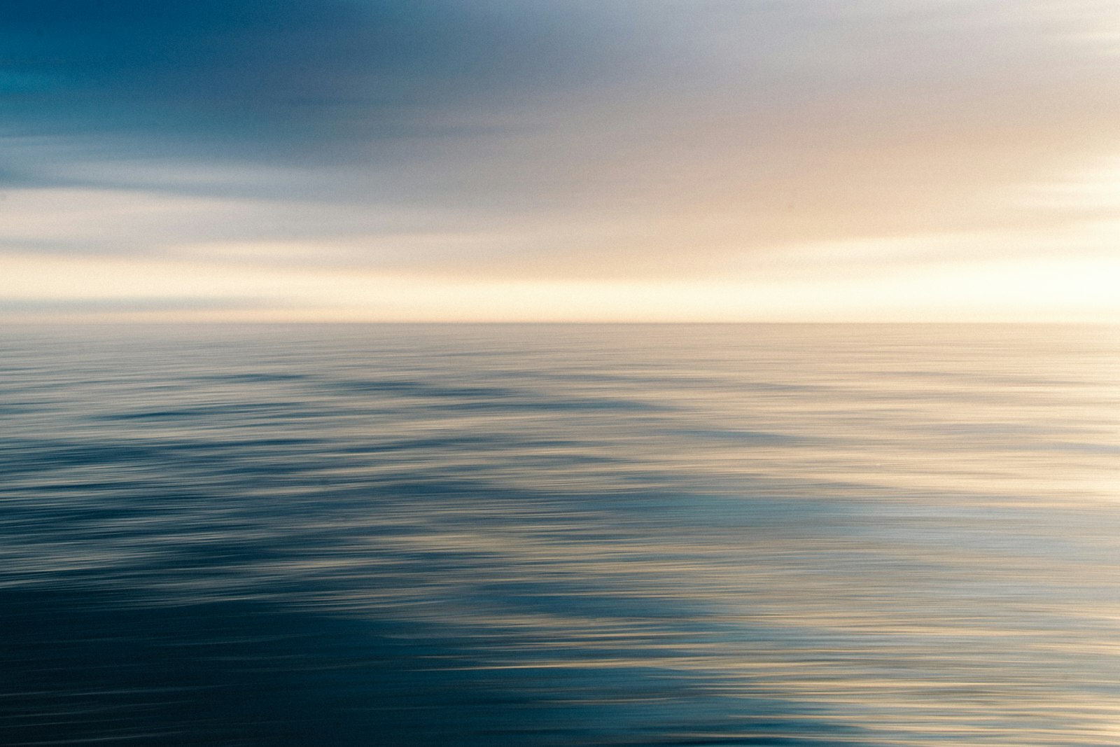 Gentle ripples stretch across open water beneath a cloudy sky, with pale light along the horizon.